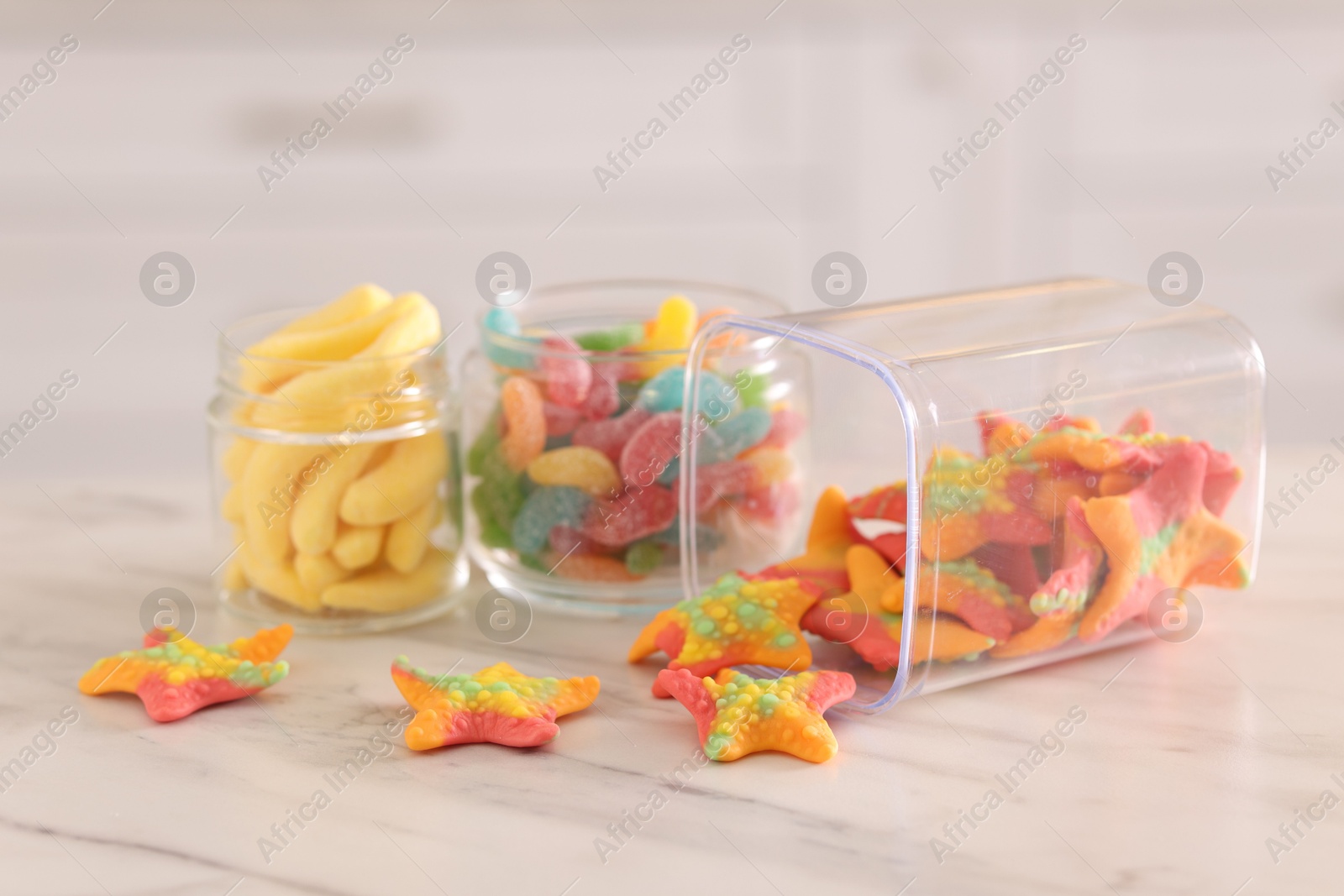 Photo of Tasty gummy candies in glass jars on white marble table