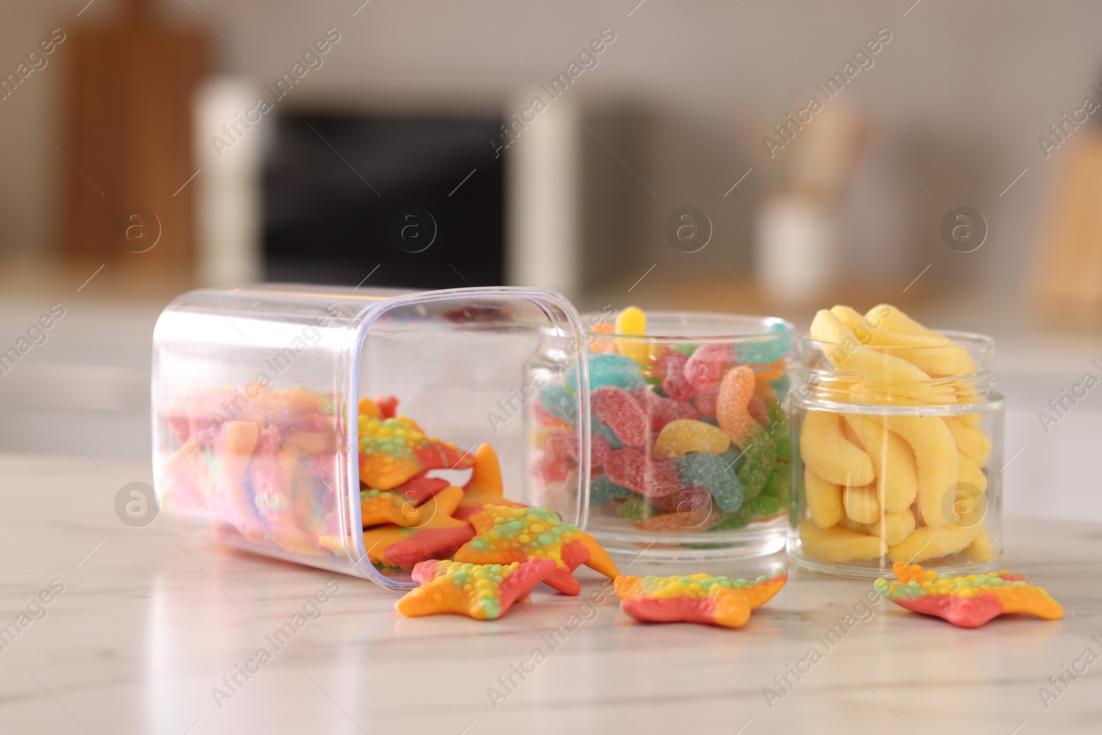 Photo of Tasty gummy candies in glass jars on white marble table