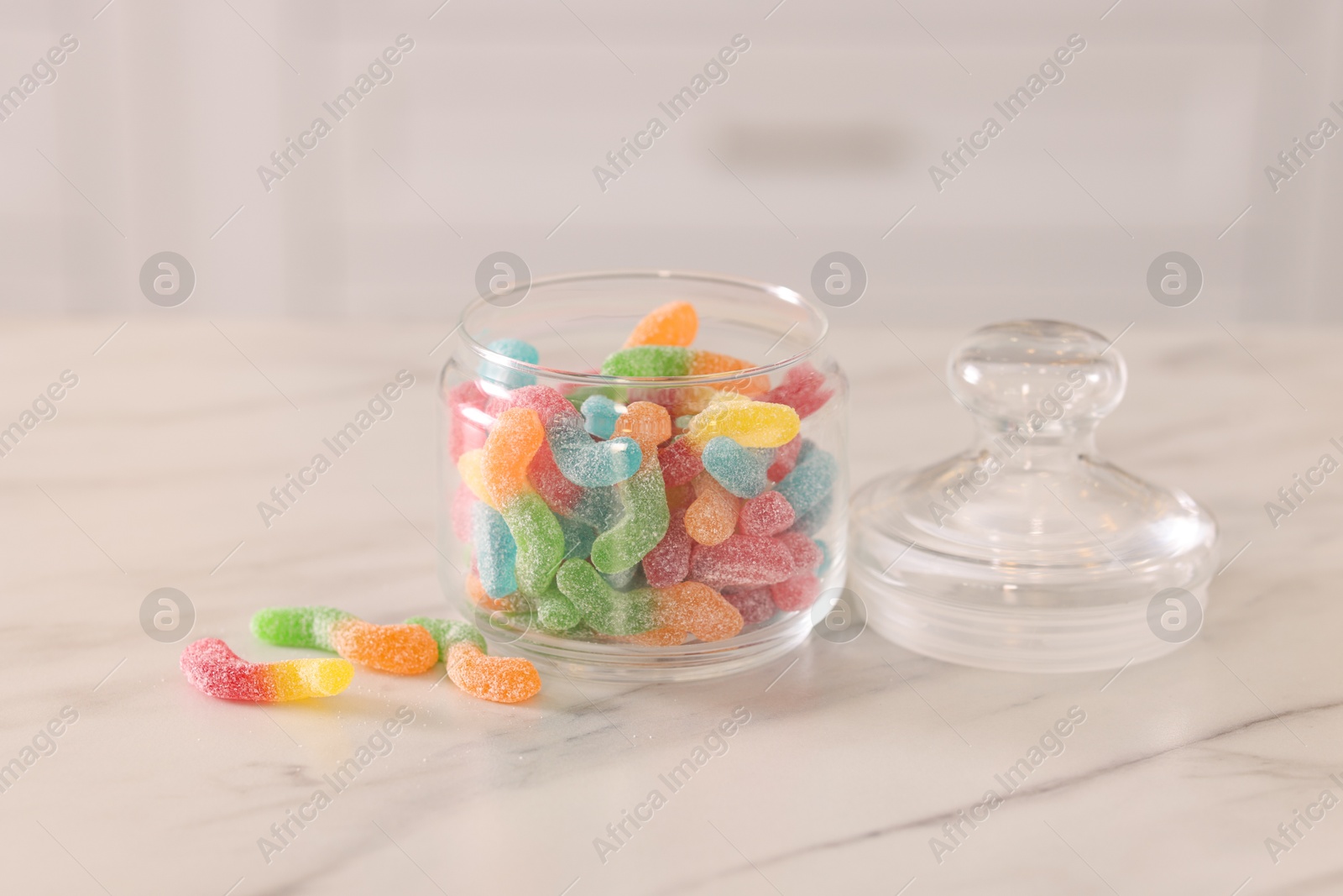 Photo of Gummy candies in glass jar on white marble table indoors