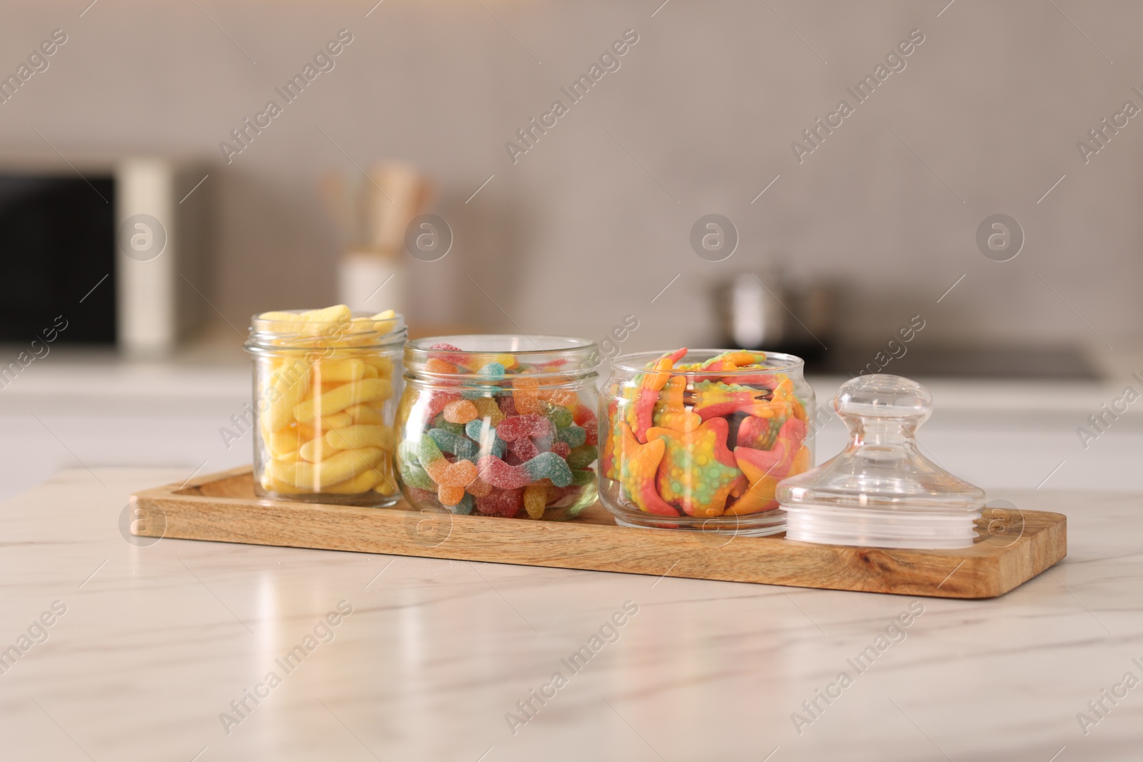 Photo of Tasty gummy candies in glass jars on white marble table