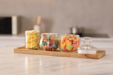 Photo of Tasty gummy candies in glass jars on white marble table