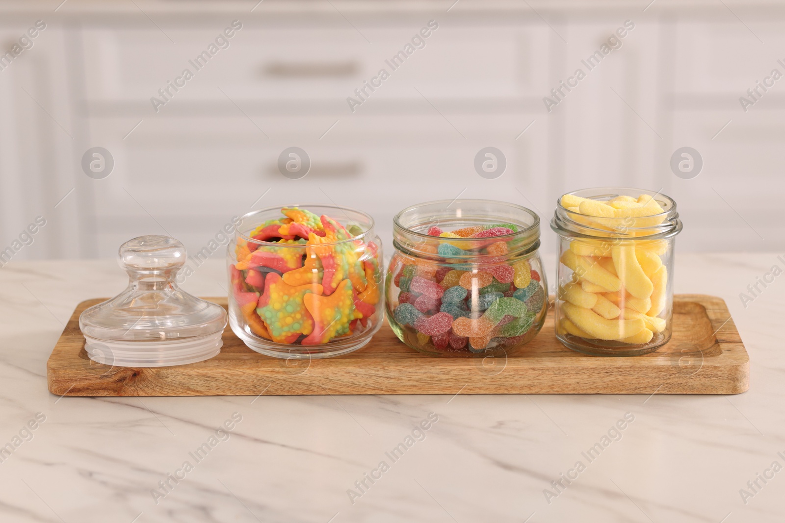 Photo of Tasty gummy candies in glass jars on white marble table