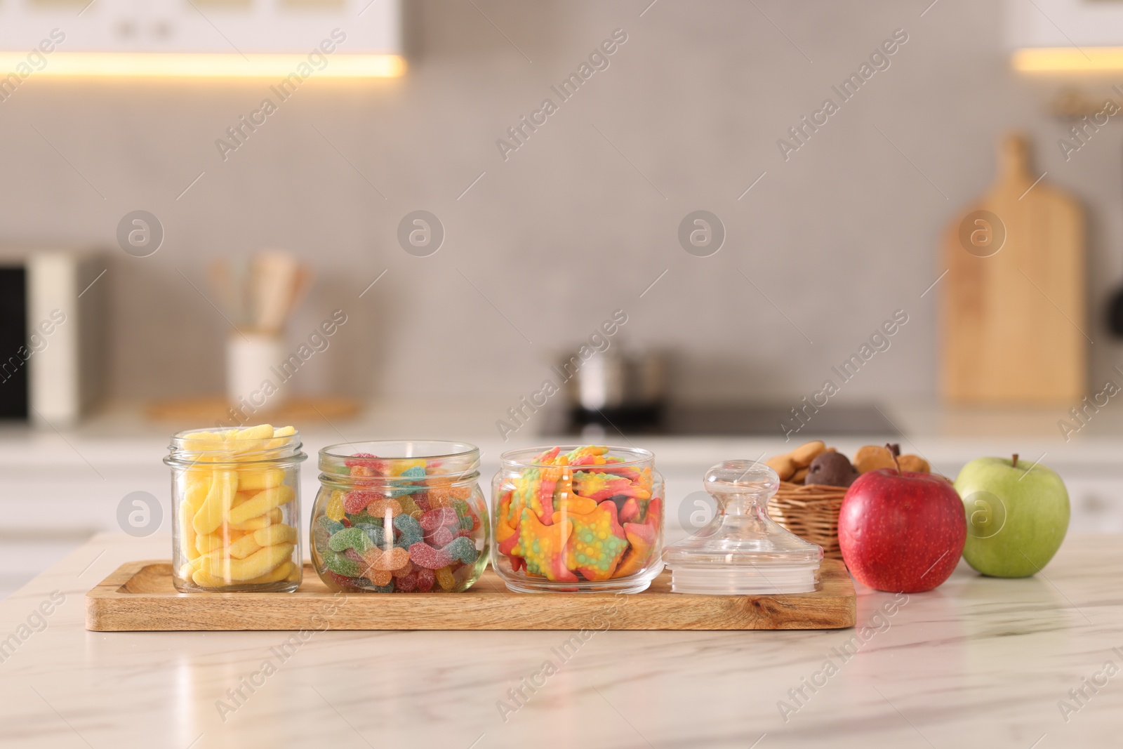 Photo of Tasty gummy candies, apples and cookies on white marble table