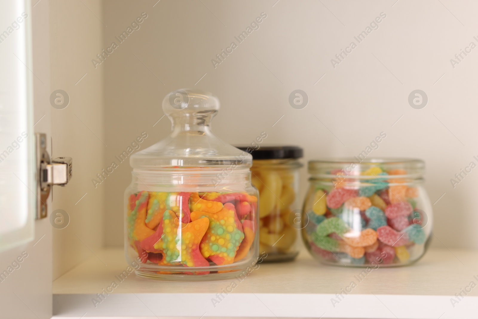 Photo of Tasty gummy candies in jars on shelf