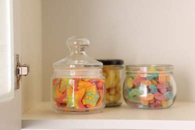 Photo of Tasty gummy candies in jars on shelf