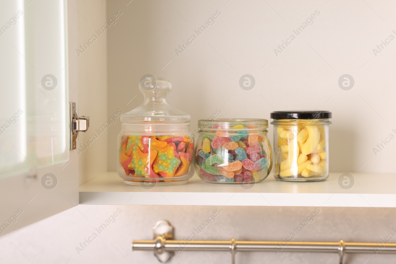 Photo of Tasty gummy candies in jars on shelf