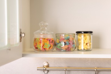 Photo of Tasty gummy candies in jars on shelf