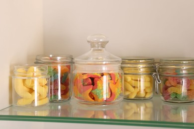 Photo of Tasty gummy candies in jars on shelf