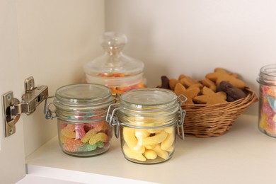 Photo of Tasty gummy candies in jars and cookies on shelf