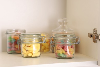 Photo of Tasty gummy candies in jars on shelf