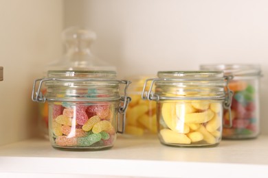 Photo of Tasty gummy candies in jars on shelf, closeup