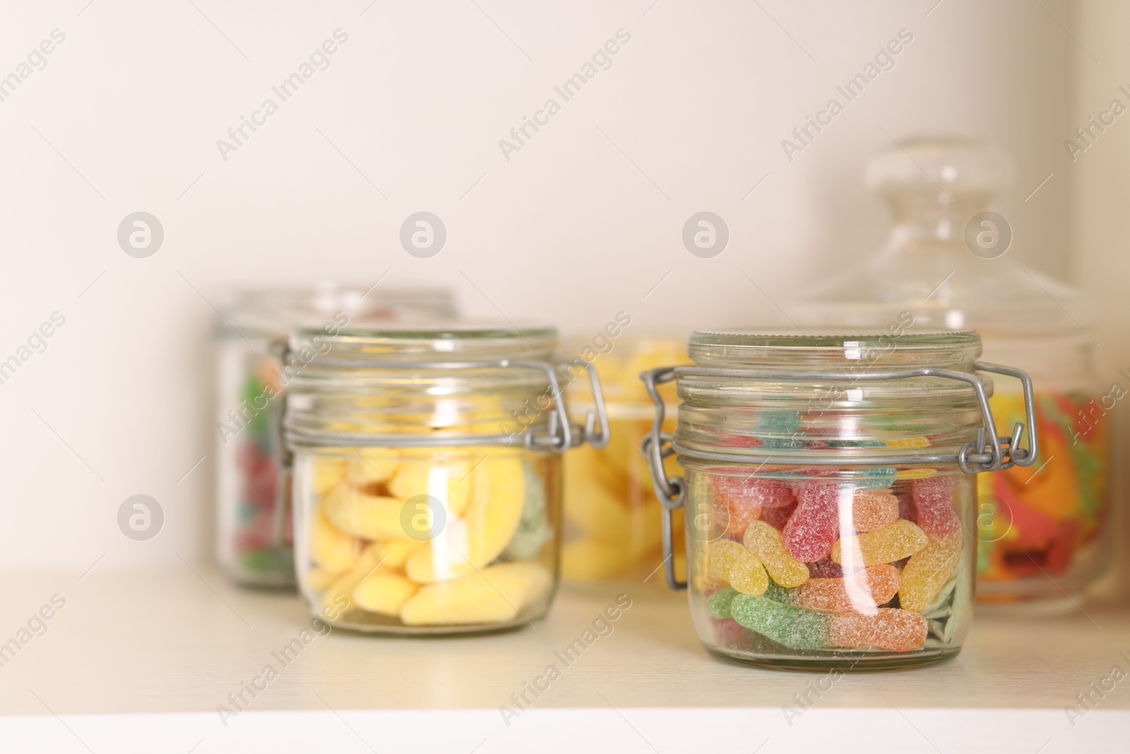 Photo of Tasty gummy candies in jars on shelf, closeup