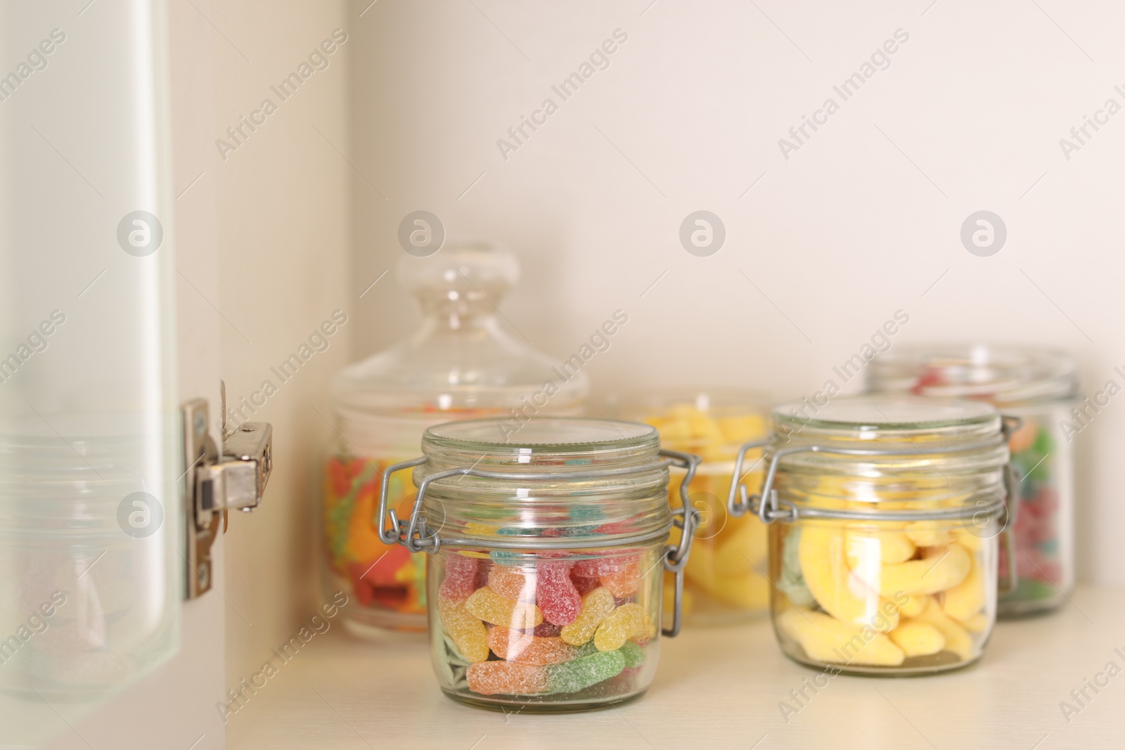 Photo of Tasty gummy candies in jars on shelf