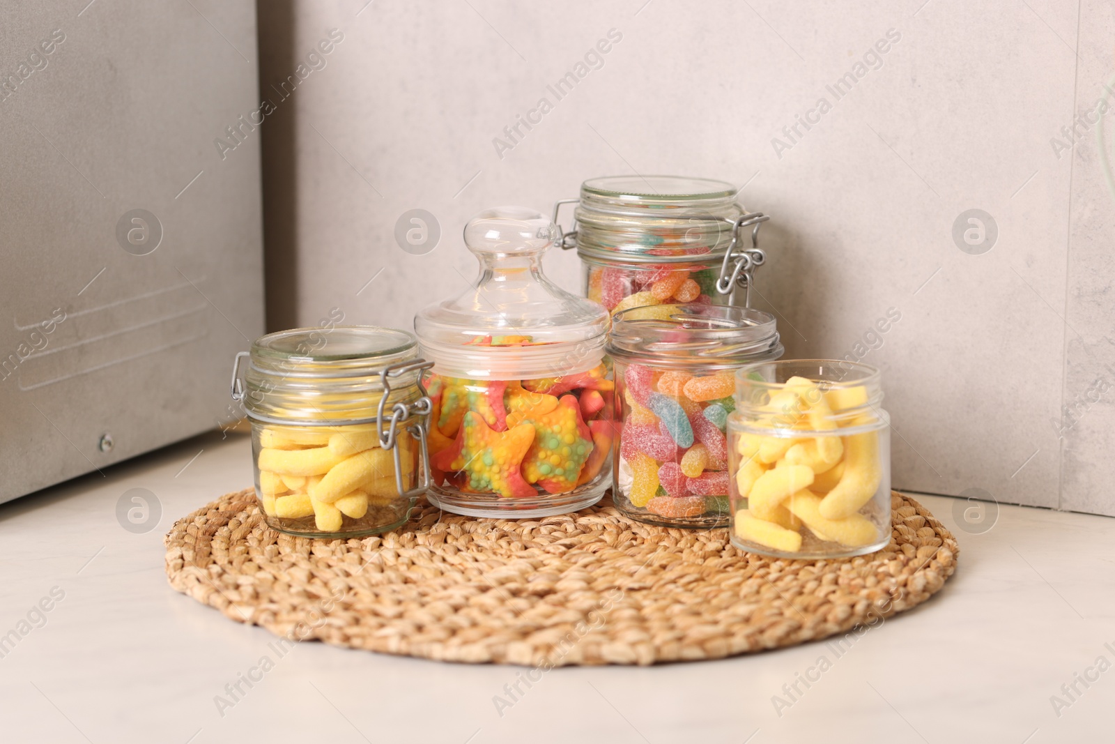 Photo of Tasty gummy candies in glass jars on white table