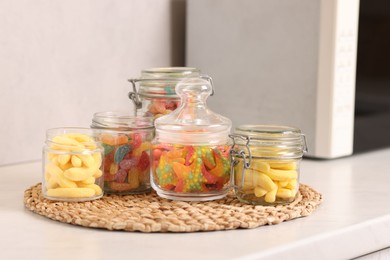 Photo of Tasty gummy candies in glass jars on white table