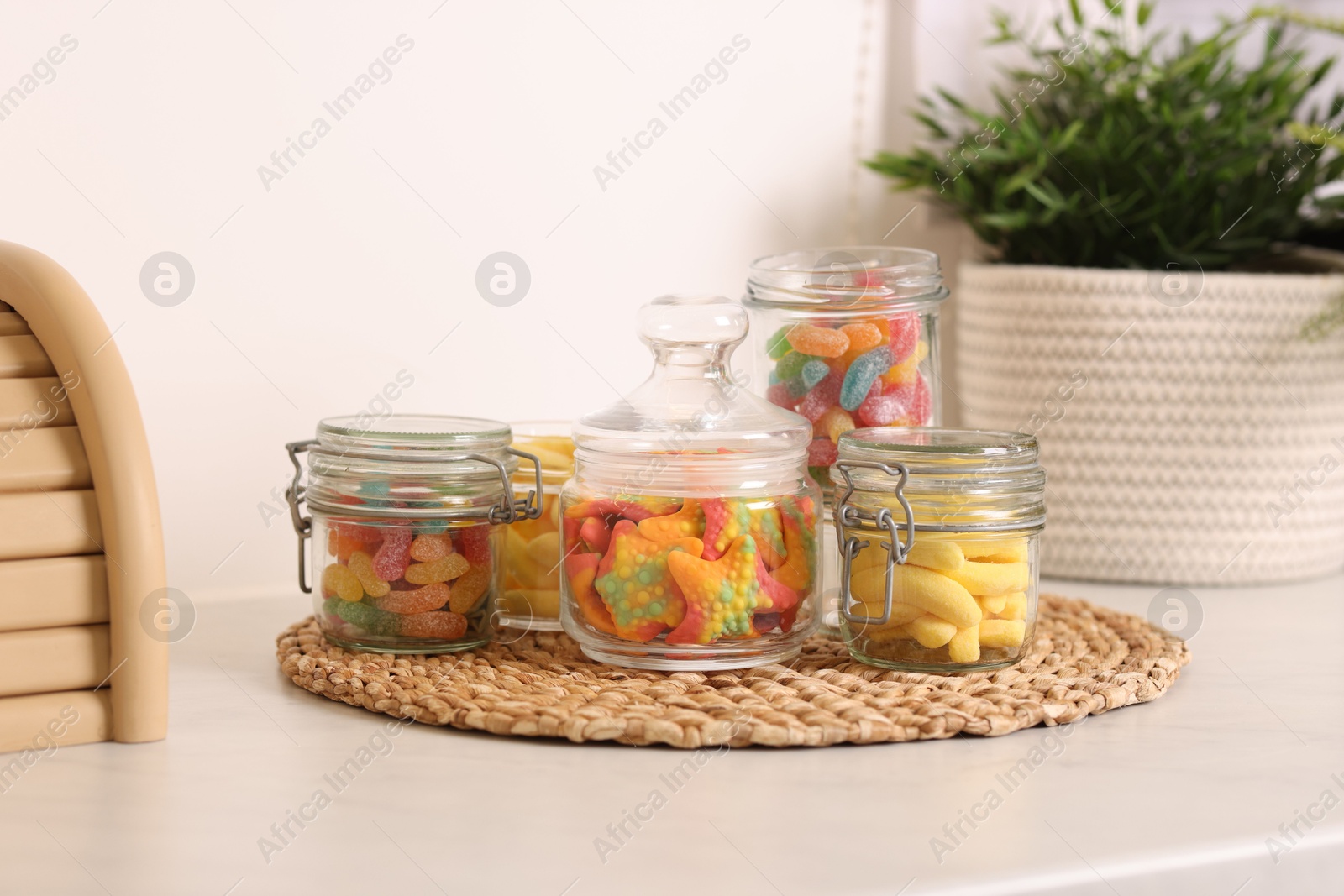 Photo of Tasty gummy candies in glass jars on white table