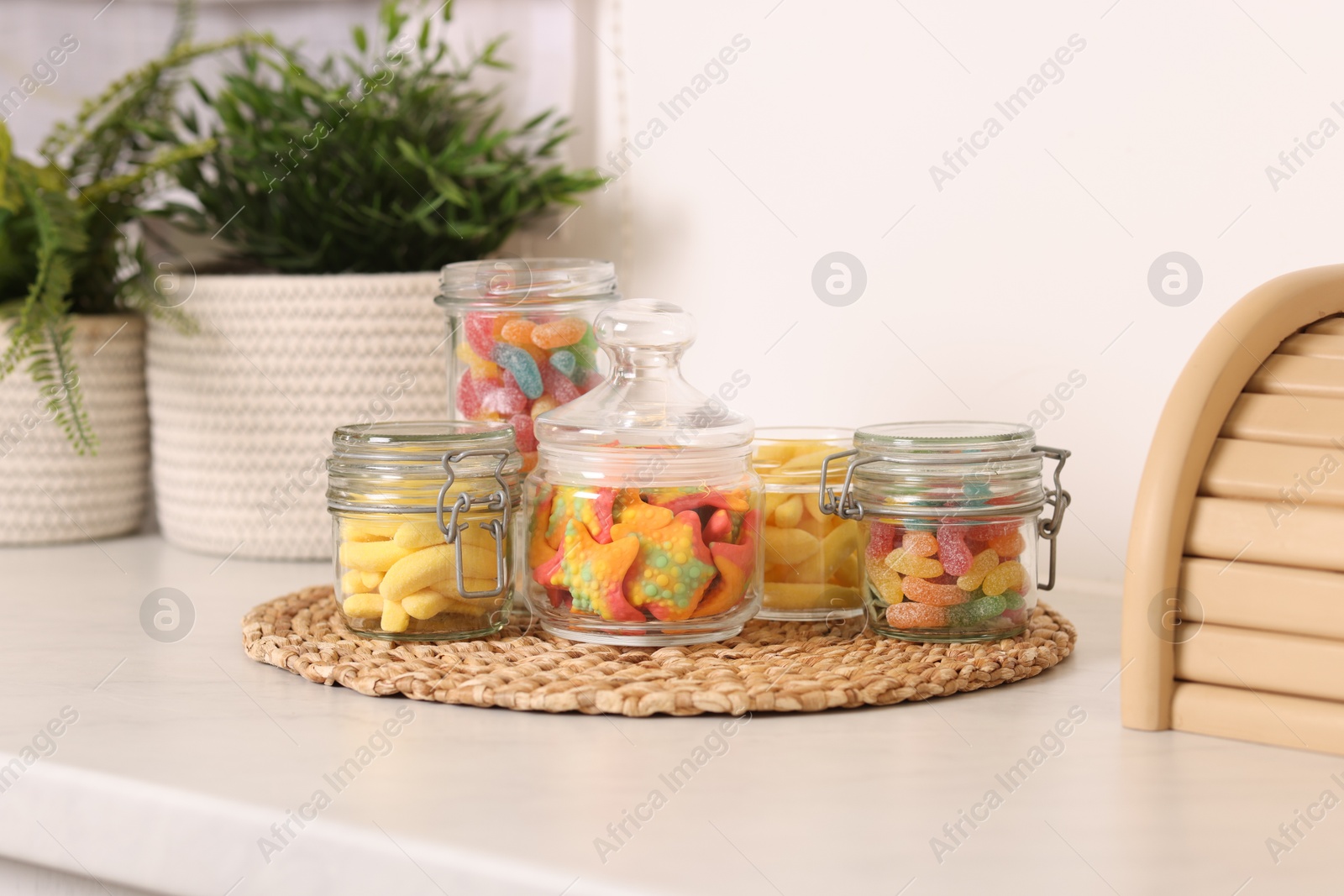 Photo of Tasty gummy candies in glass jars on white table