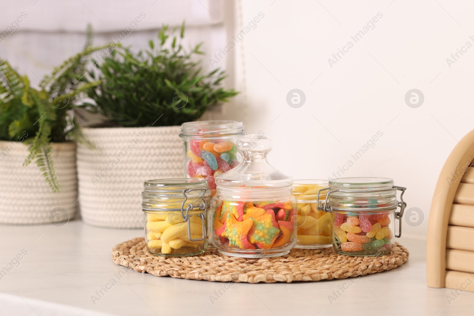 Photo of Tasty gummy candies in glass jars on white table