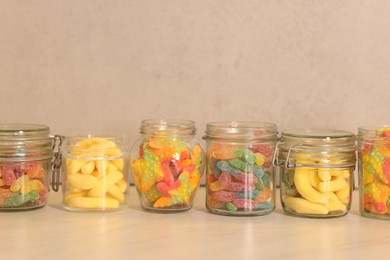 Photo of Tasty gummy candies in glass jars on light table