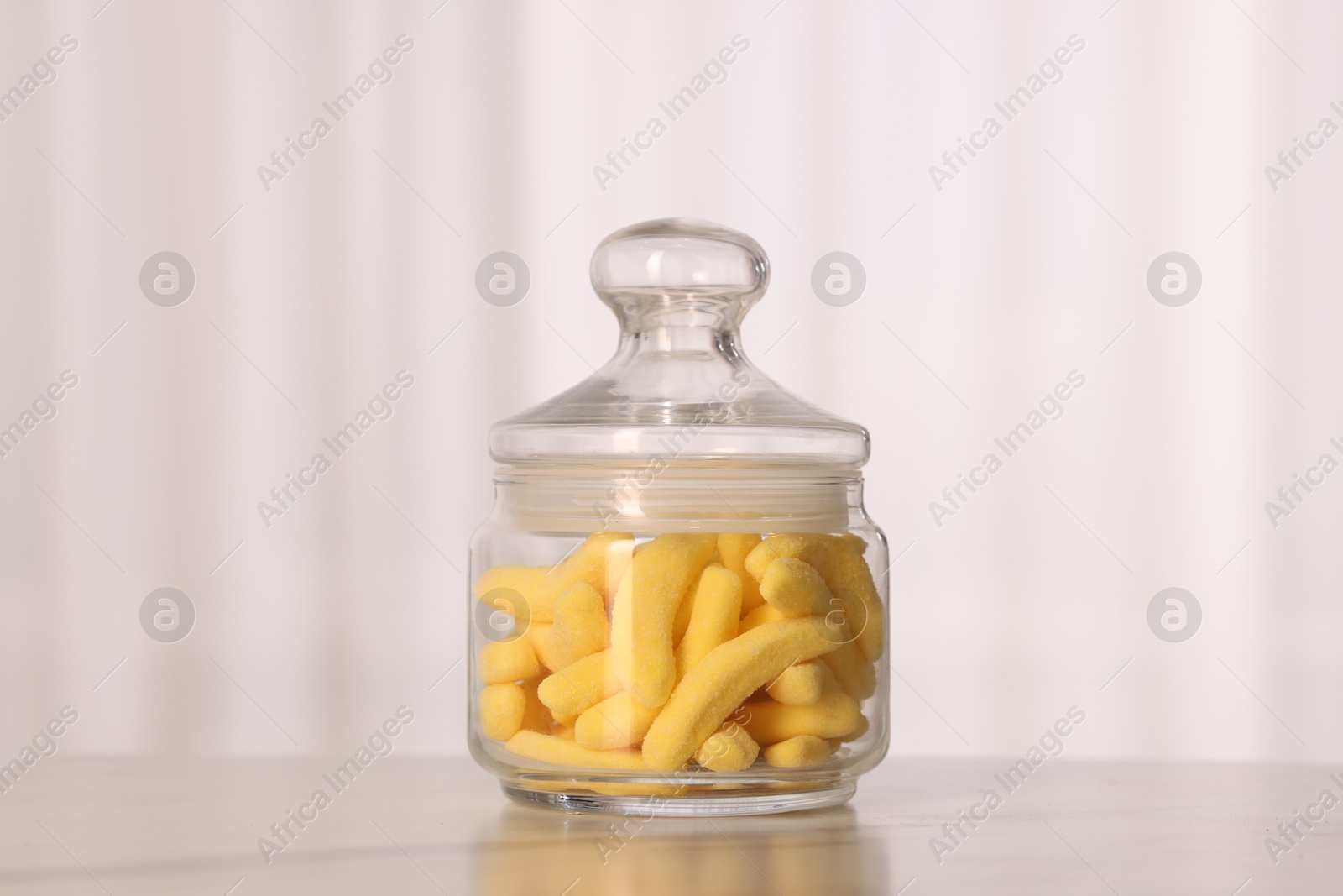 Photo of Gummy candies in glass jar on white marble table indoors