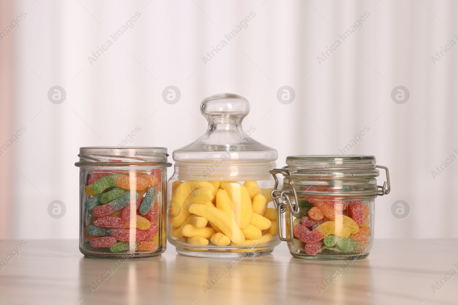 Photo of Tasty gummy candies in glass jars on white marble table