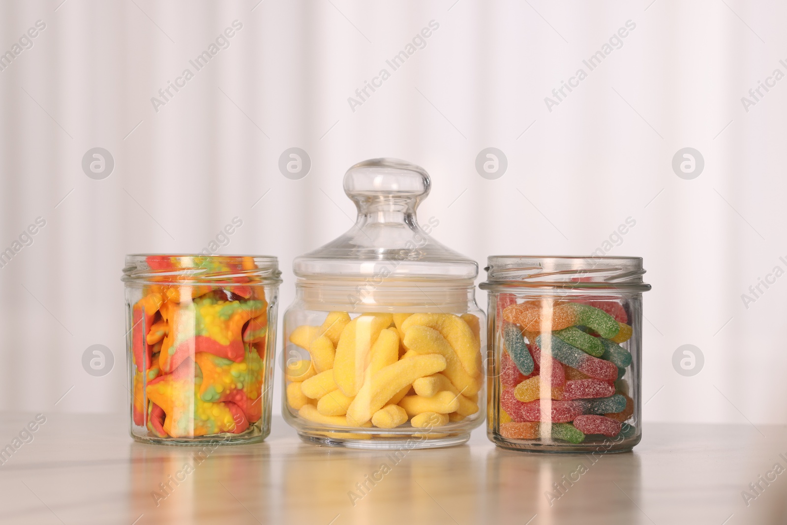 Photo of Tasty gummy candies in glass jars on white marble table