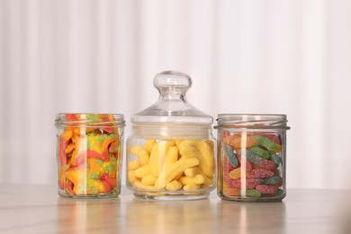 Photo of Tasty gummy candies in glass jars on white marble table