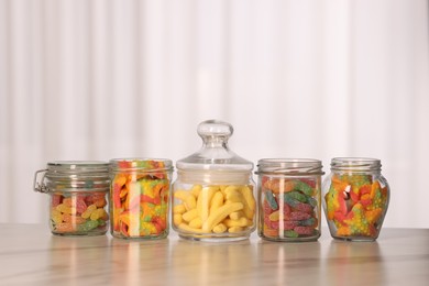 Photo of Tasty gummy candies in glass jars on white marble table