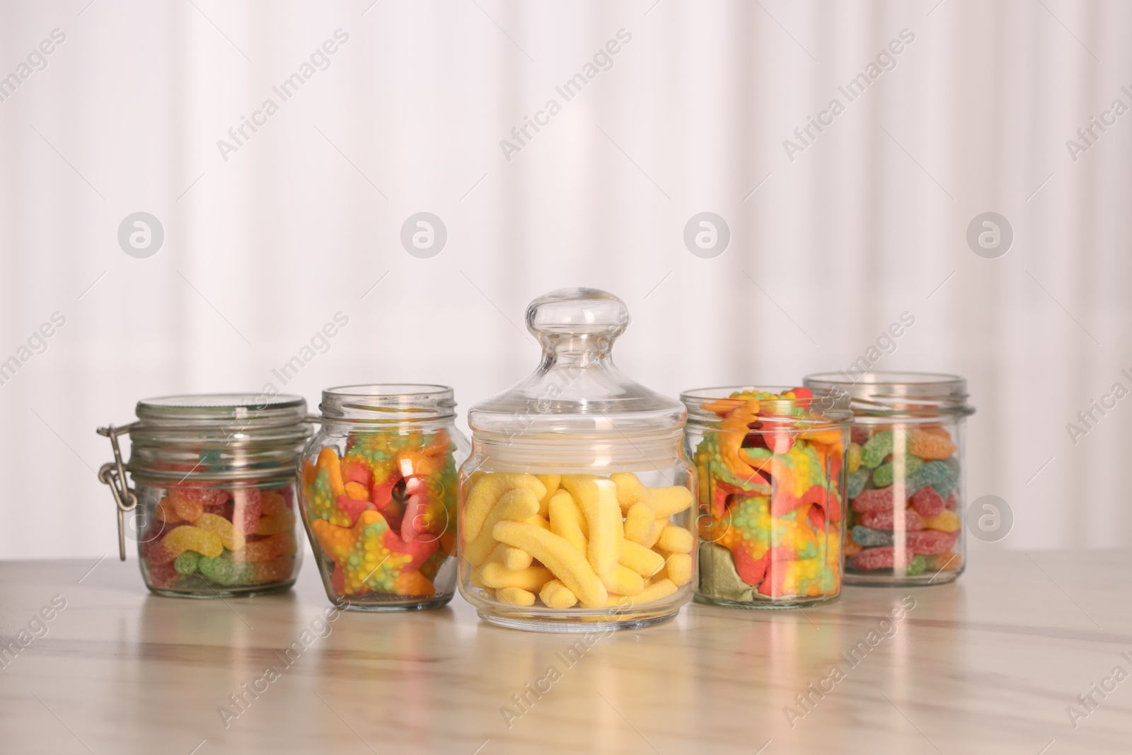 Photo of Tasty gummy candies in glass jars on white marble table