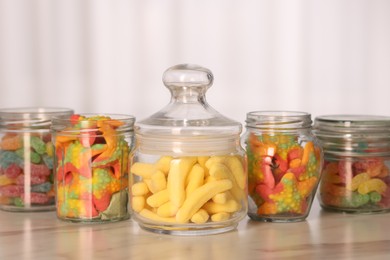 Photo of Tasty gummy candies in glass jars on white marble table, closeup