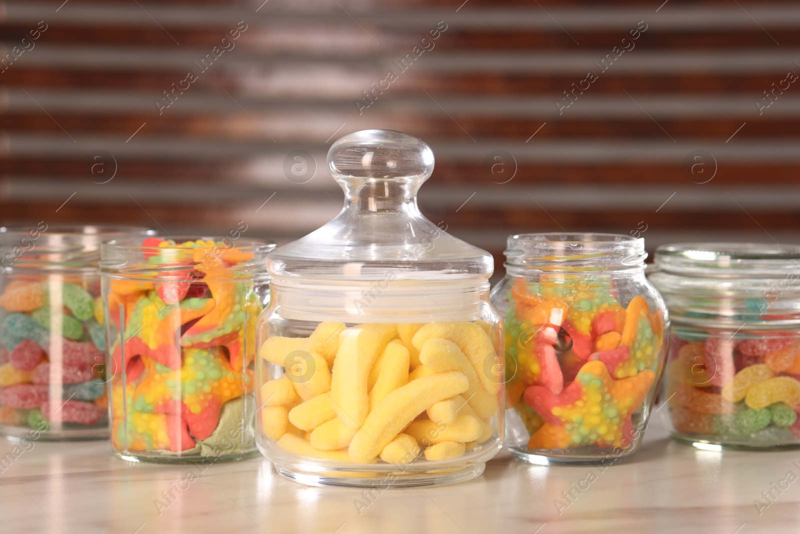 Photo of Tasty gummy candies in glass jars on white marble table, closeup