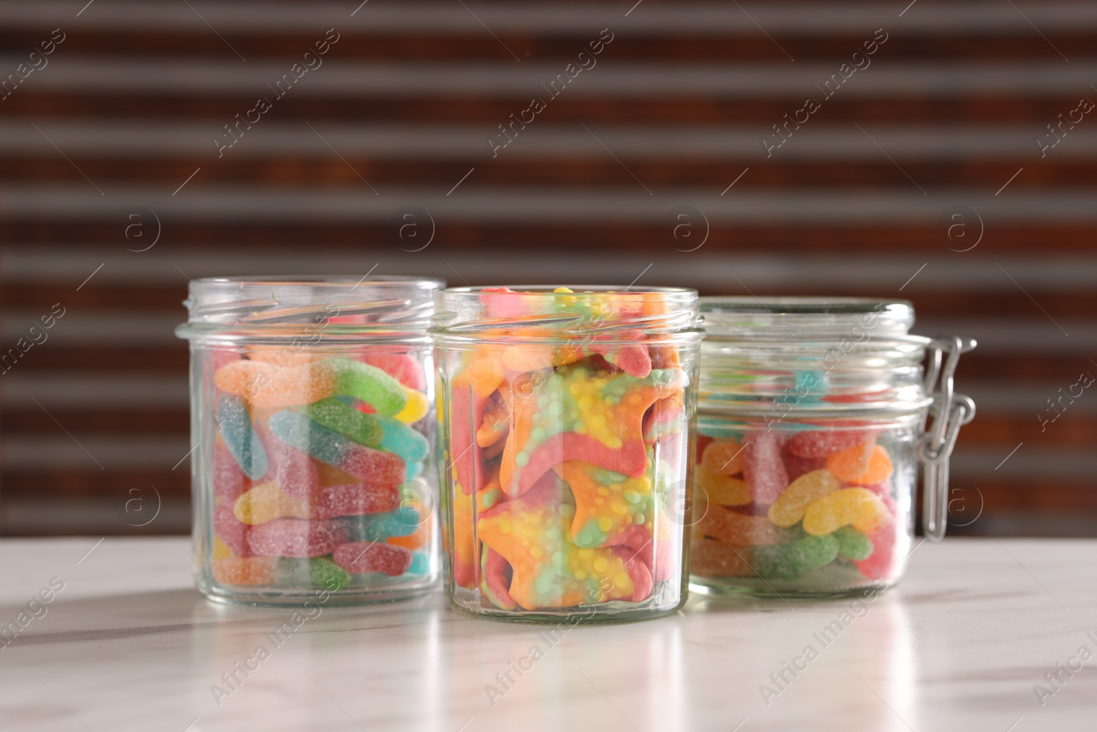 Photo of Tasty gummy candies in glass jars on white marble table