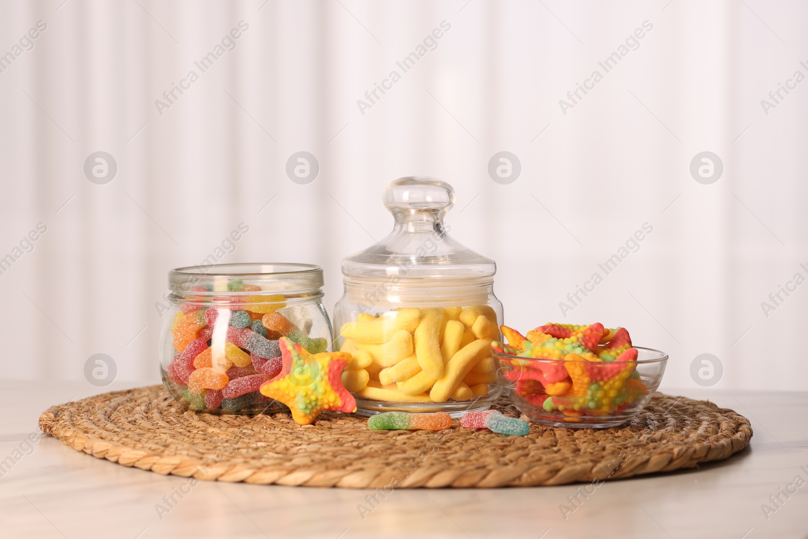 Photo of Tasty gummy candies in glass jars on white table