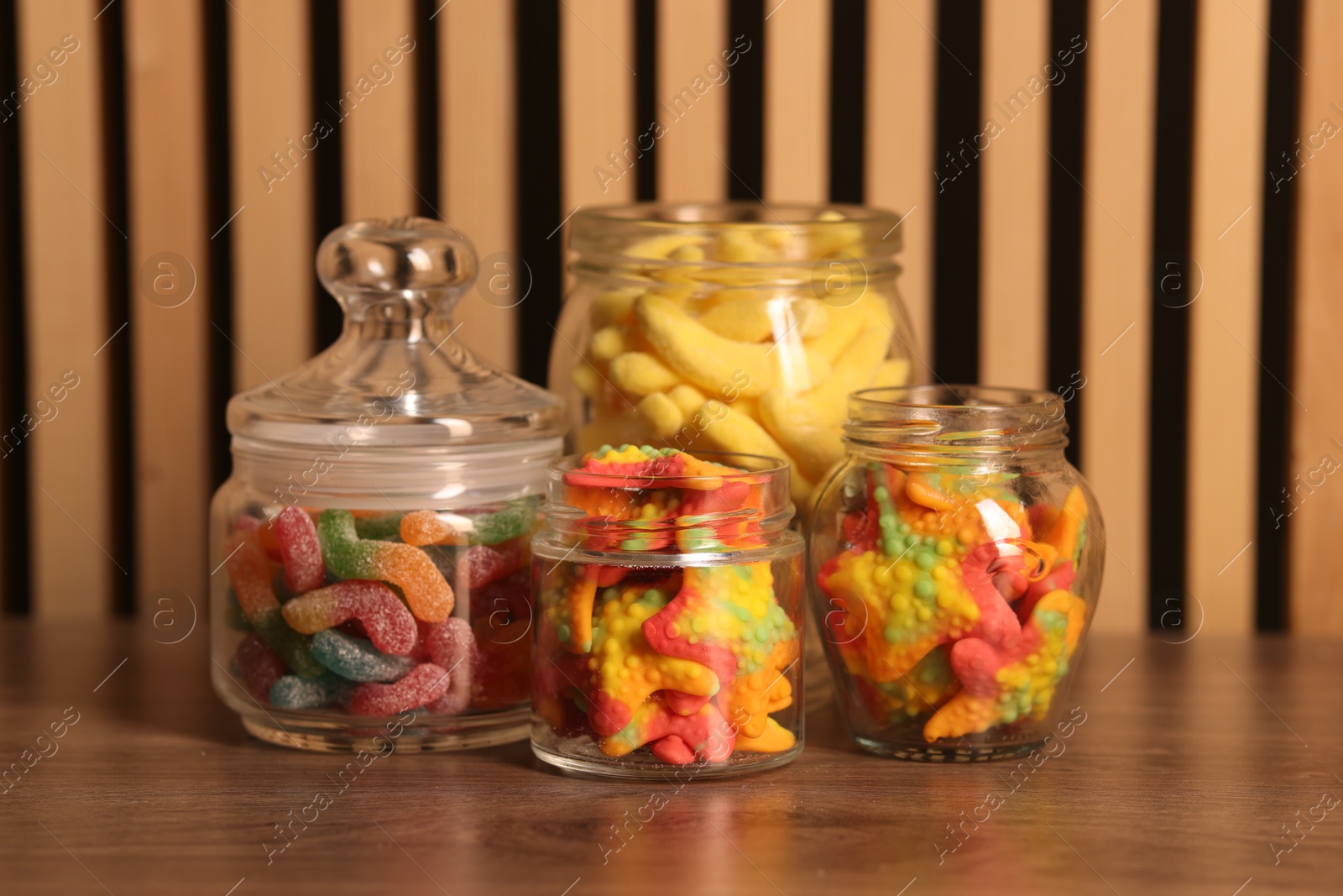 Photo of Tasty gummy candies in glass jars on wooden table