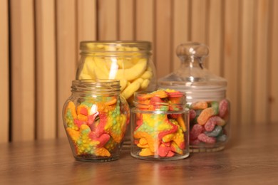 Photo of Tasty gummy candies in glass jars on wooden table