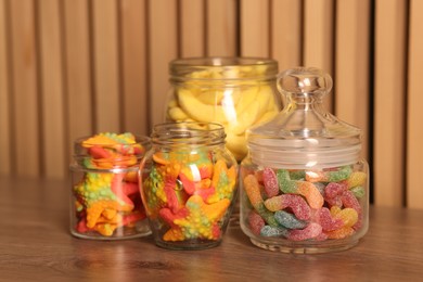 Photo of Tasty gummy candies in glass jars on wooden table, closeup