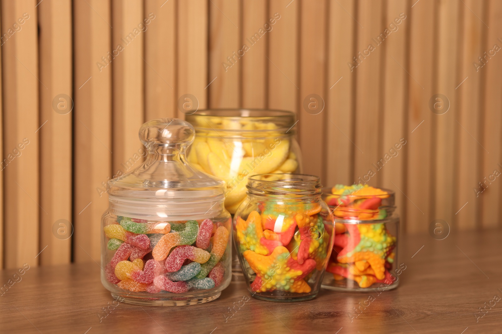 Photo of Tasty gummy candies in glass jars on wooden table