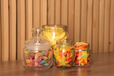 Photo of Tasty gummy candies in glass jars on wooden table