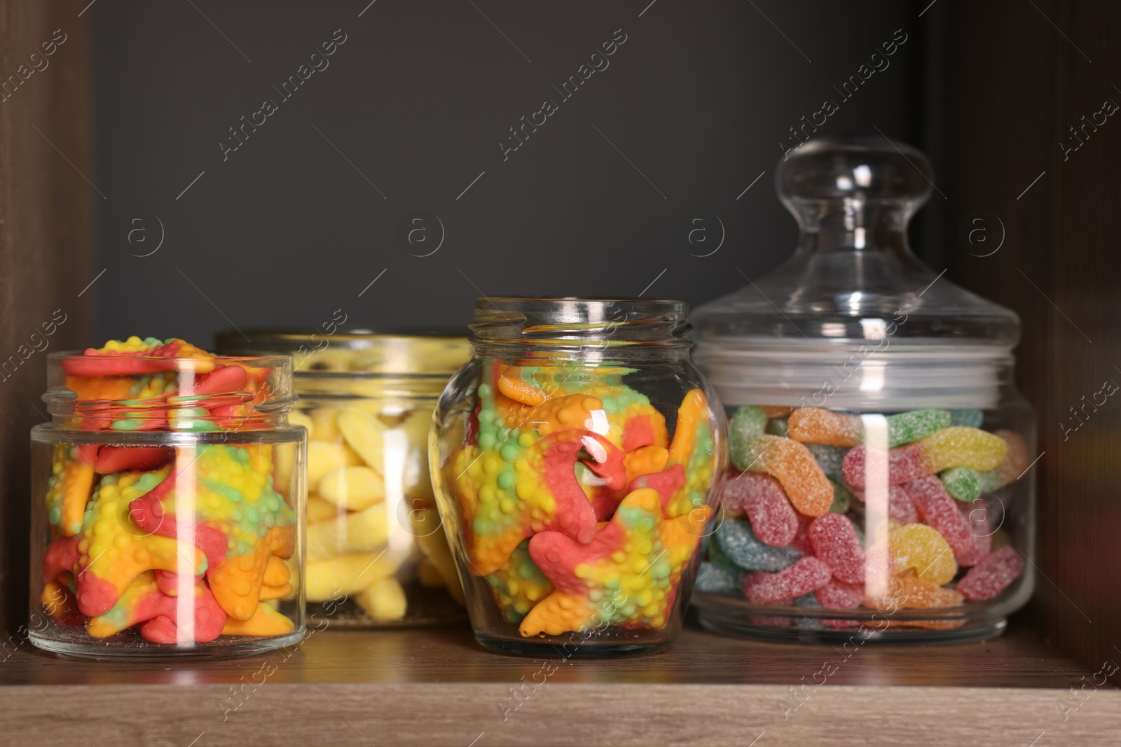 Photo of Tasty gummy candies in jars on shelf, closeup