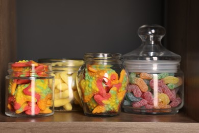 Photo of Tasty gummy candies in jars on shelf, closeup