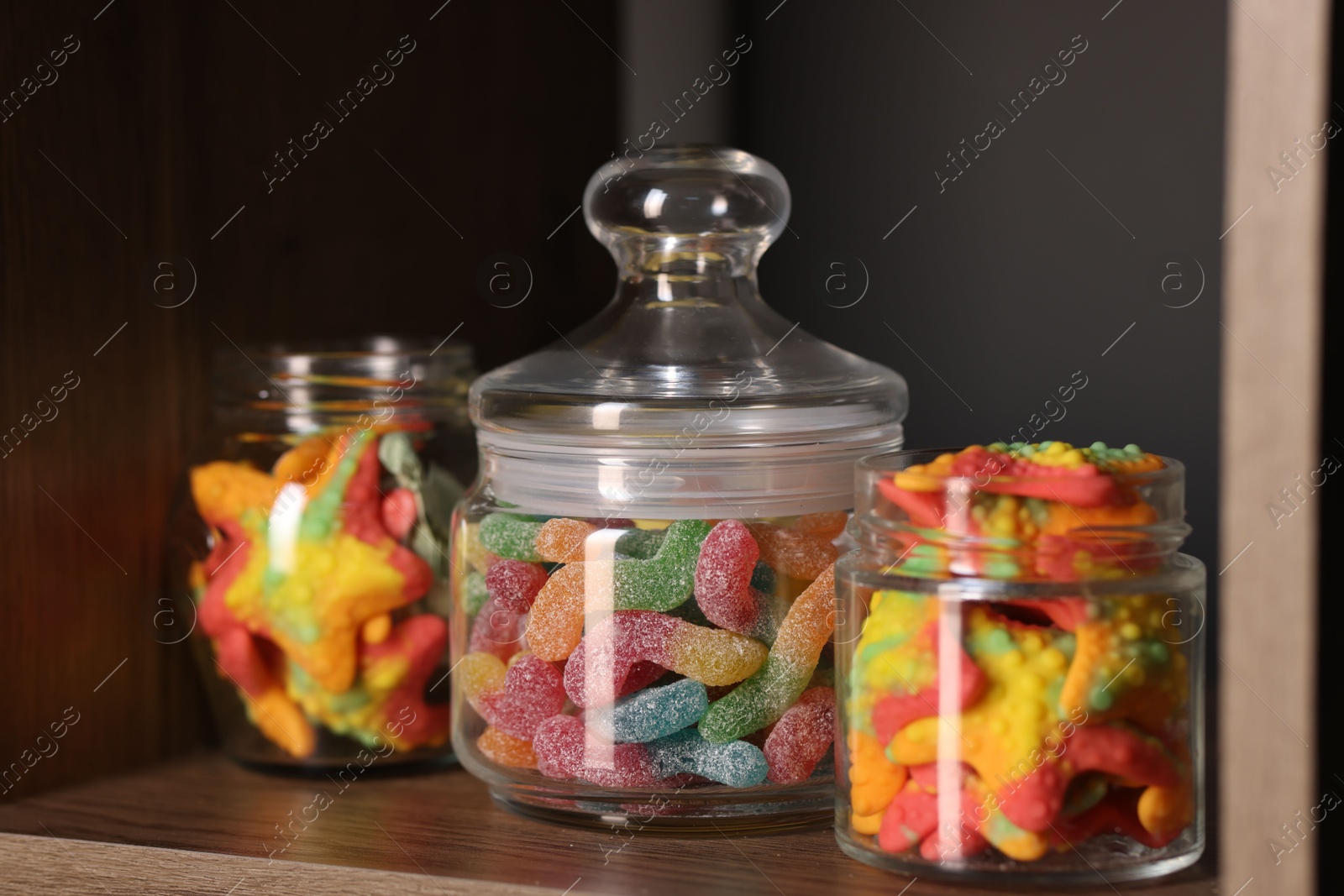 Photo of Tasty gummy candies in jars on shelf, closeup