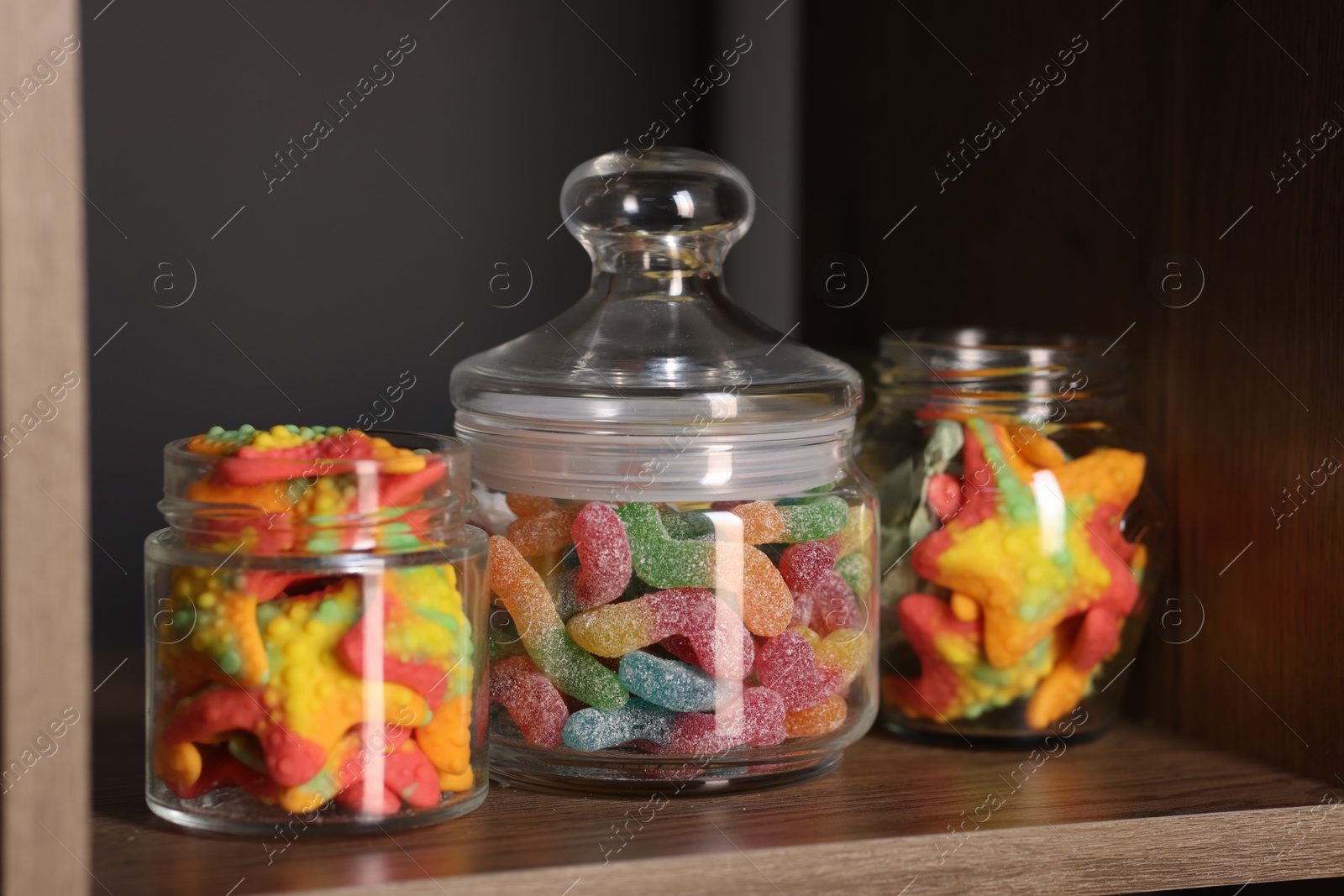 Photo of Tasty gummy candies in jars on shelf, closeup