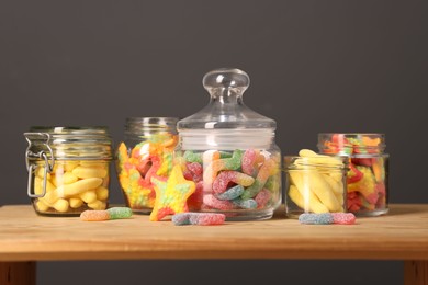 Photo of Tasty gummy candies in glass jars on wooden table against grey background