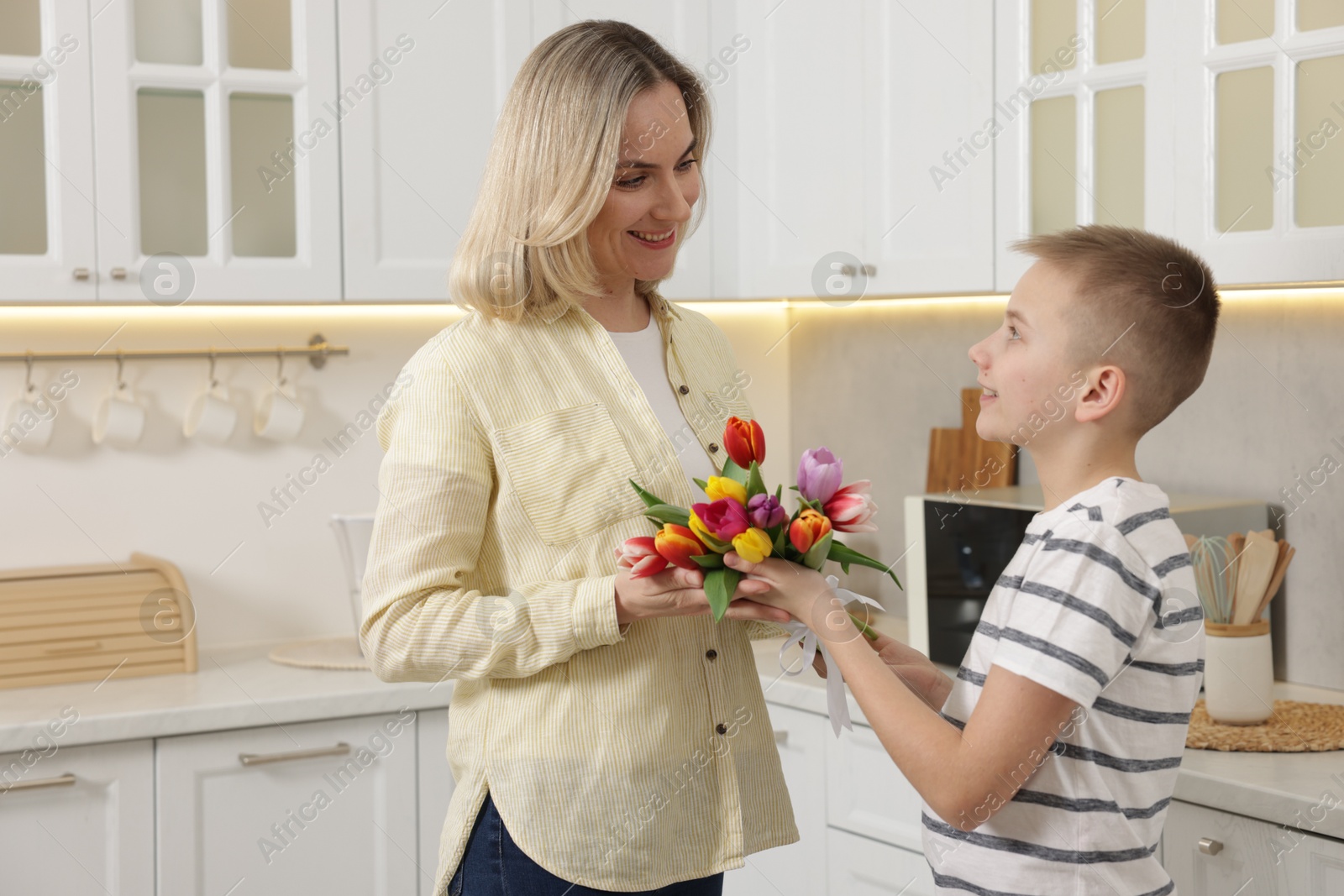 Photo of Happy Mother's Day. Son greeting his mom with flowers in kitchen