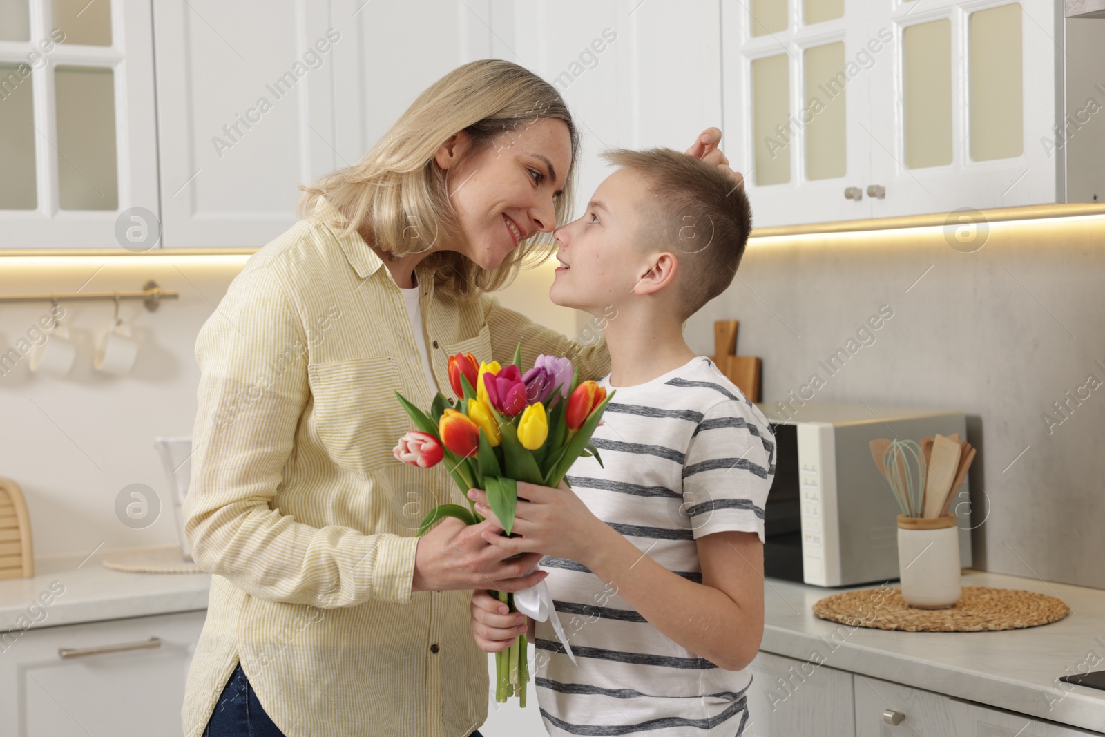 Photo of Happy Mother's Day. Son greeting his mom with flowers in kitchen