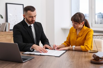 Client signing notarial paperwork during meeting with lawyer at wooden desk indoors