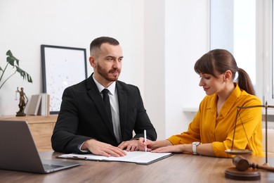 Client signing notarial paperwork during meeting with lawyer at wooden desk indoors