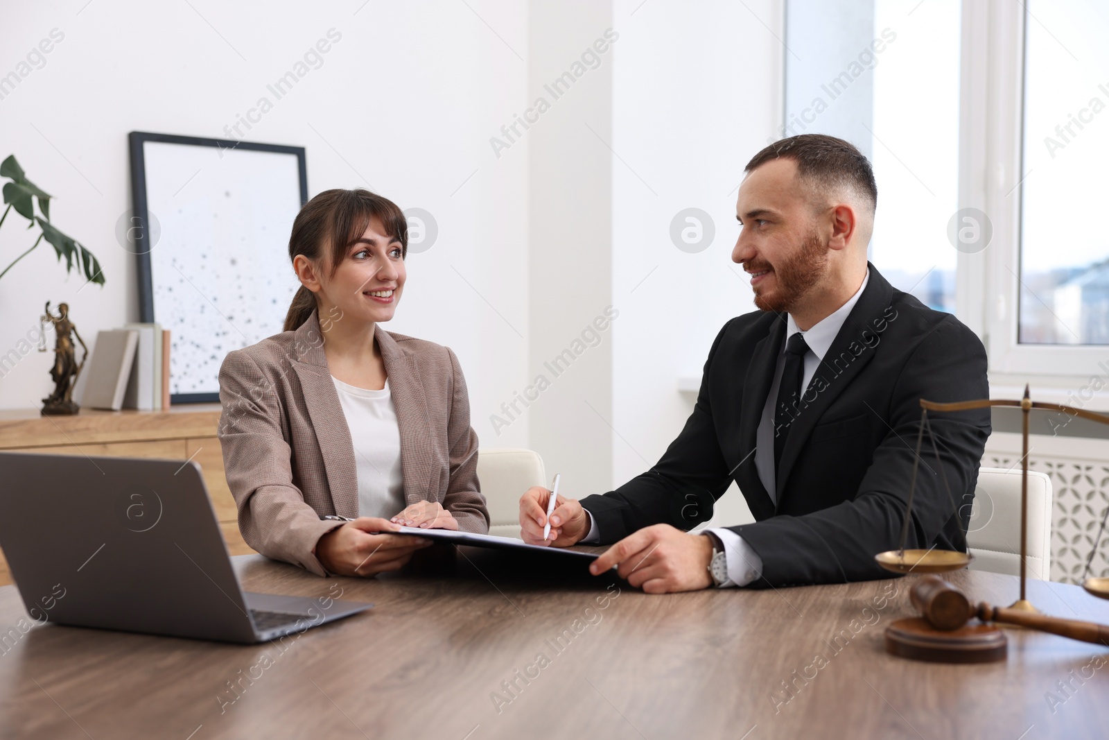 Photo of Client signing notarial paperwork during meeting with lawyer at wooden desk indoors