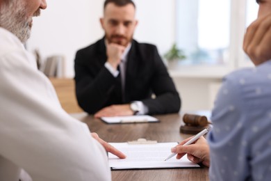 Photo of Man and woman having meeting with professional notary at wooden desk indoors