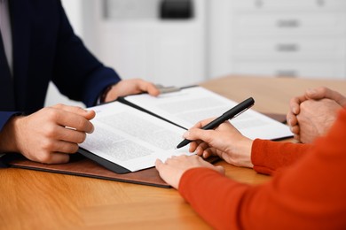 Client signing notarial paperwork during meeting with lawyer at wooden desk indoors, closeup